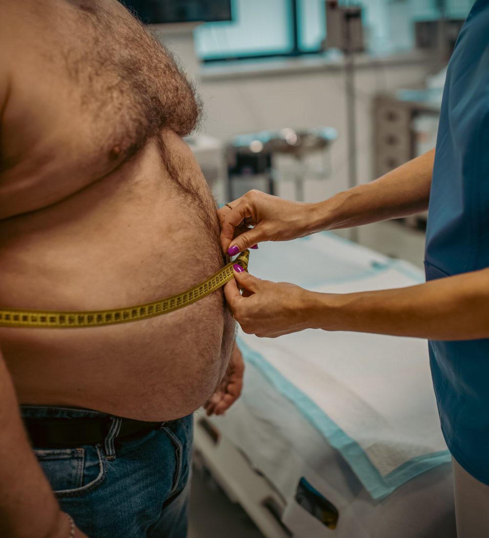 Female doctor measuring waist of overweight patient using a tape measure. Obesity affecting middle-aged men's health. Concept of health risks of overwight and obesity.